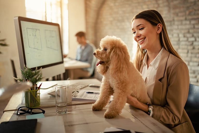 Happy businesswoman enjoying with her dog while working in the o